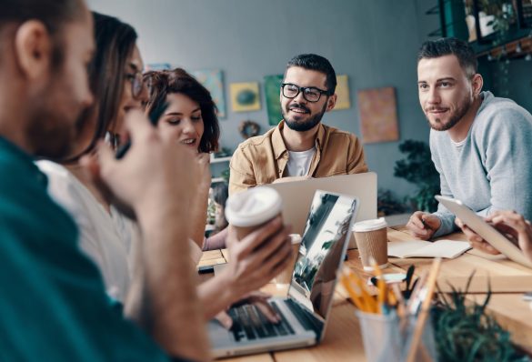 Collaboration is a key to best results. Group of young modern people in smart casual wear discussing something and smiling while working in the creative office