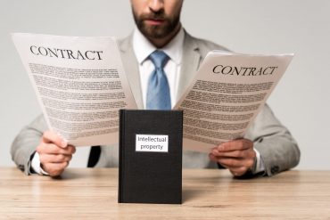 cropped view of businessman reading contracts near book with intellectual property title isolated on